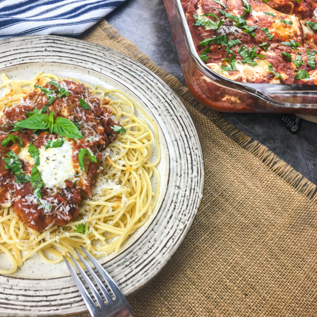 Chicken Parmesan spaghetti on a plate with a fork beside it and the baking dish in the background