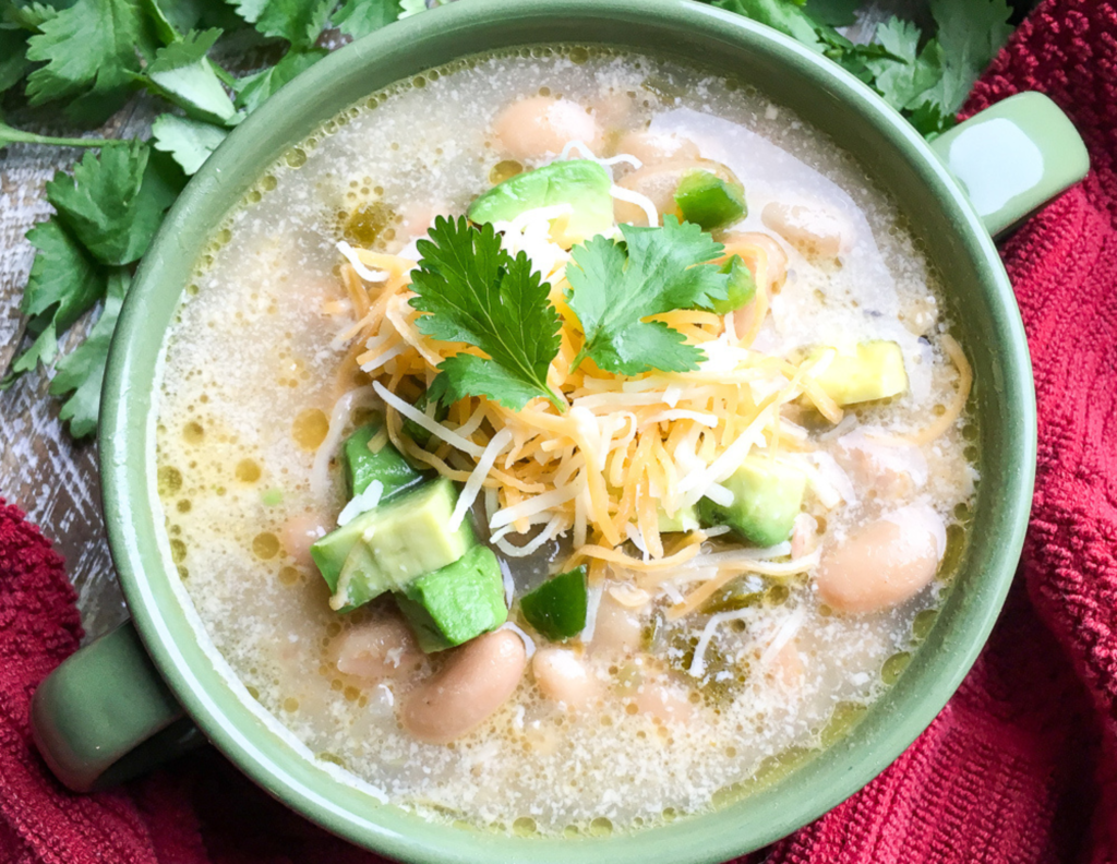 Slow cooker white chili chicken in a green bowl with coriander beside it
